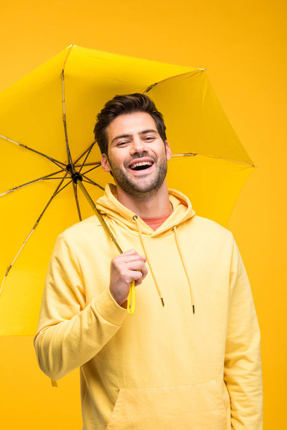 handsome man holding umbrella and laughing isolated on yellow - Valokuva, kuva