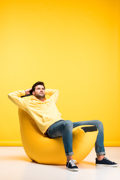 man with Hands Behind Back relaxing on bean bag chair on yellow - Valokuva, kuva