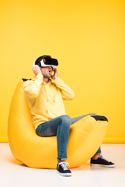 excited man on bean bag chair in virtual reality headset on yellow - Photo, Image