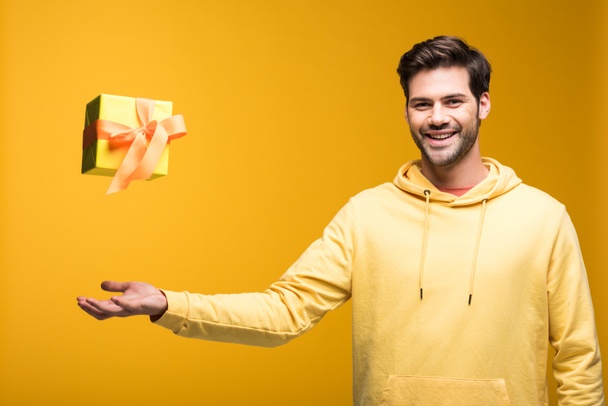 красивый улыбчивый мужчина бросает в воздух подарок на желтом
 - Фото, изображение
