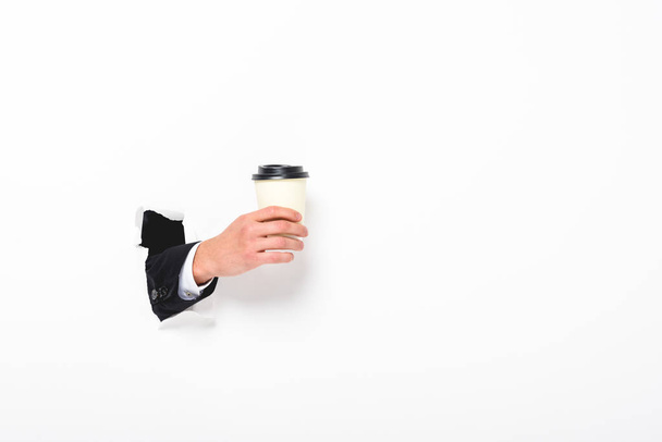 Przycięte widok człowieka trzymając kawę, aby przejść z otworu w ścianie na białym  - Zdjęcie, obraz