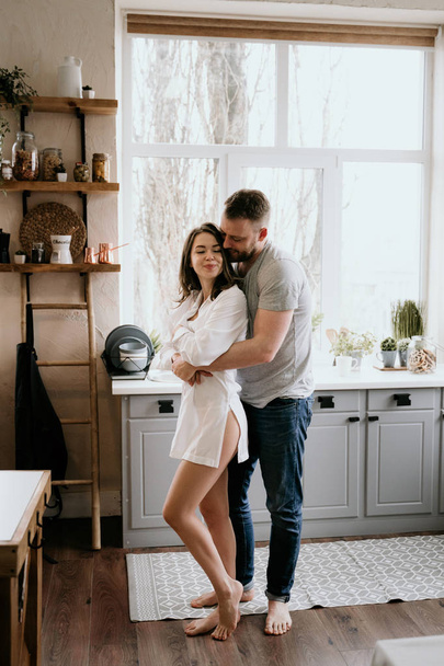 Romantic young couple cooking together in the kitchen. The girl in the white shirt. Breakfast together. - Foto, Imagem