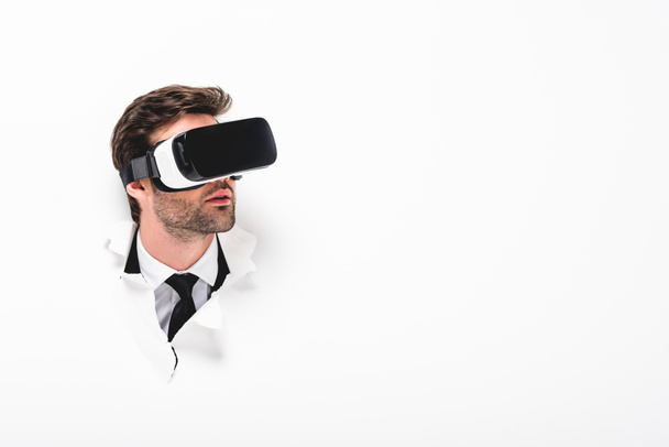 man in Virtual reality headset behind hole in wall on white with copy space - Foto, afbeelding