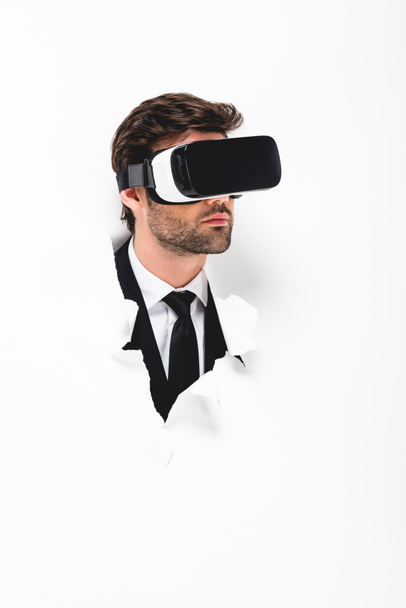 man in suit and Virtual reality headset behind hole in wall on white - Foto, imagen