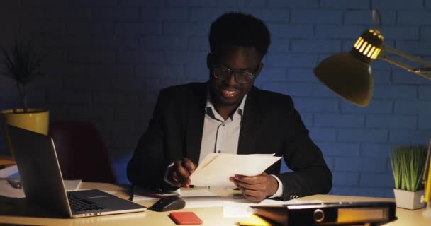 Young happy businessman reading documents at desk in night office. Man working at documents. - Materiaali, video