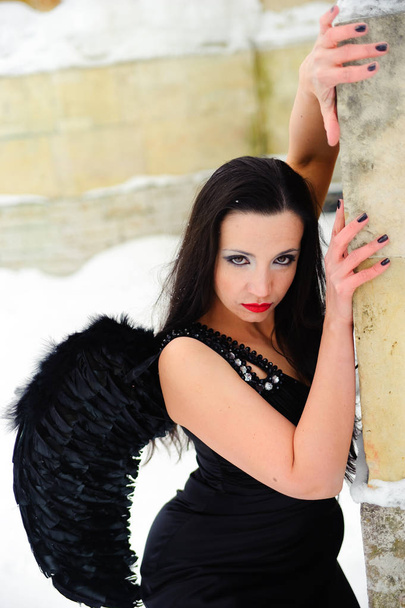 girl with black angel wings in a black dress in winter - Foto, imagen