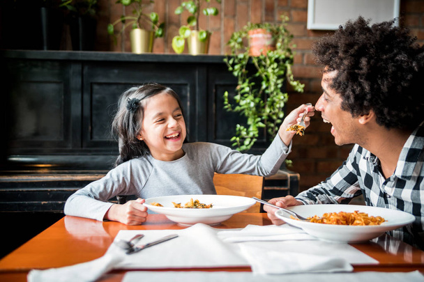 Latin dad and daughter eating together lunch at restaurant, multiethnic family having fun - Foto, afbeelding