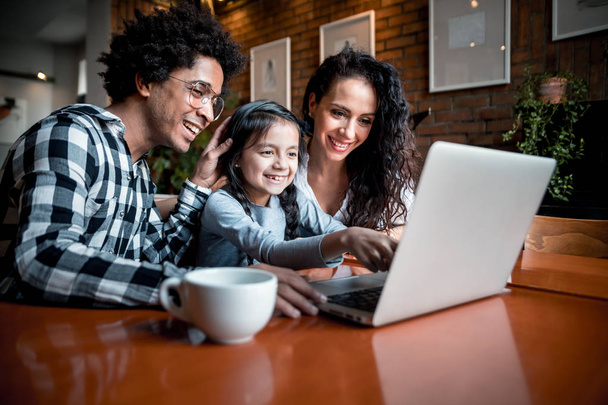 Happy multiethnic family having fun while using laptop together at restaurant - Photo, image