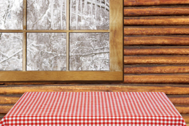 leerer Tisch im Hintergrund des Fensters. Tisch mit einer rot karierten Tischdecke im Inneren eines Landhauses. außerhalb des Winters. - Foto, Bild