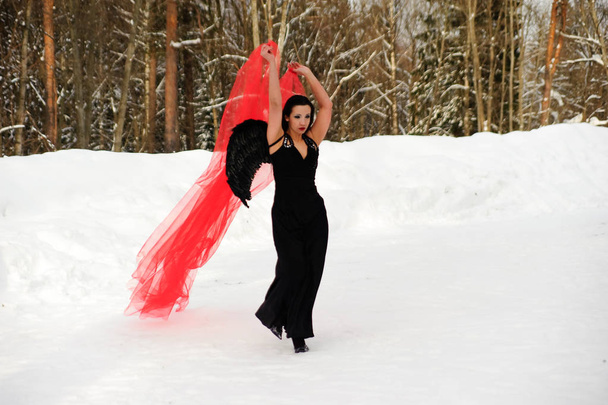 girl with black angel wings in a black dress in winter and red f - 写真・画像