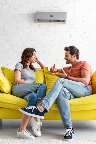усміхнений чоловік і жінка сидять на жовтому дивані під кондиціонером вдома
 - Фото, зображення
