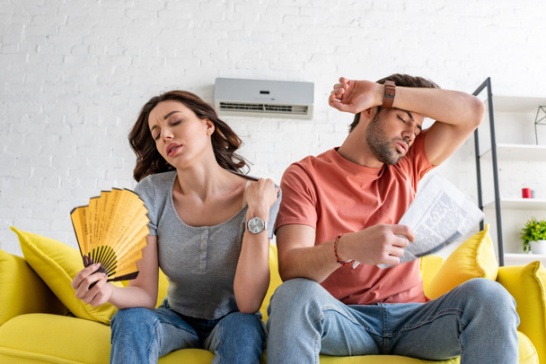 mujer bonita con ventilador de mano y hombre guapo con periódico que sufre de calor en casa
 - Foto, Imagen