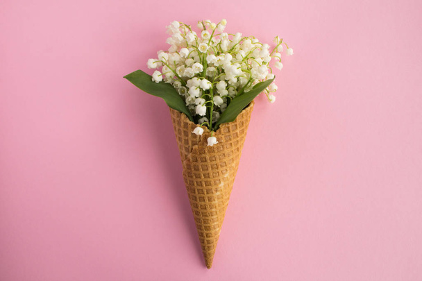 Ice cream cone with lilies of the valley  in the center of the pink  background.Top view.Copy space.Spring flowers concept. - Photo, Image