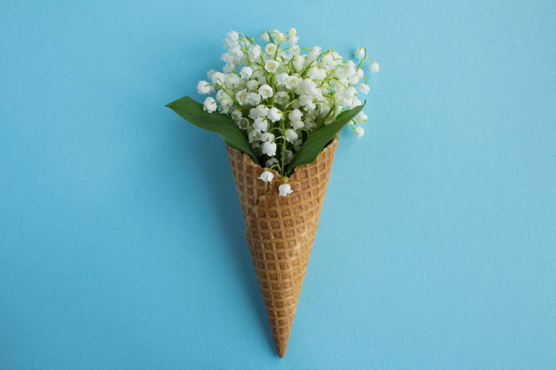 Ice cream cone with lilies of the valley  in the center of the blue background.Top view.Copy space.Spring flowers concept. - Foto, Imagen