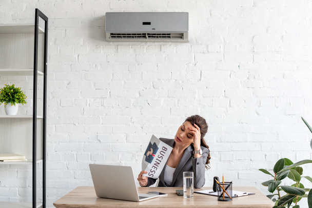 atraente empresária acenando jornal enquanto sentado no local de trabalho sob ar condicionado
 - Foto, Imagem