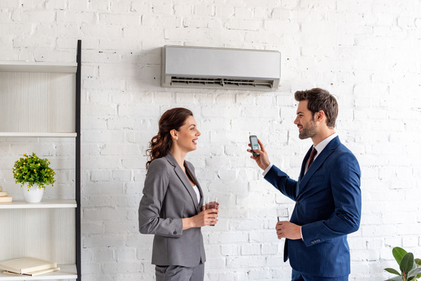 Lächelnde Geschäftsleute reden, während sie im Büro unter Klimaanlage stehen - Foto, Bild