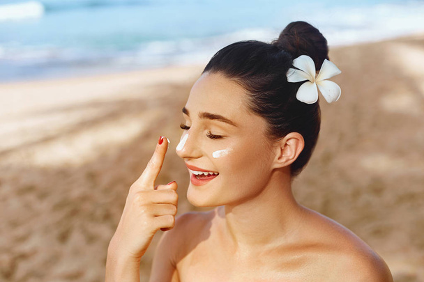 Όμορφη γυναίκα χαμόγελο εφαρμόζοντας αντηλιακή κρέμα στο πρόσωπο. Skincare. Προστασία από τον ήλιο. Αντηλιακό. Θηλυκό σε λεκέ από καπέλο ενυδατική λοσιόν στο δέρμα - Φωτογραφία, εικόνα