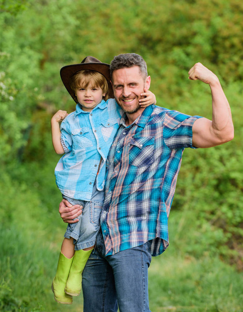 kid in rubber boots. happy dad in forest. human and nature. family day. happy earth day. Eco farm. small boy help muscular father in farming. father and son in cowboy hat on ranch. stronger together - 写真・画像