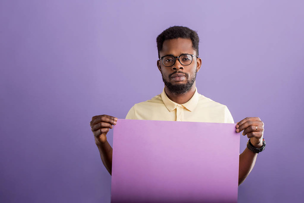 Picture of young african american man holding blank board on violet background - Foto, Bild