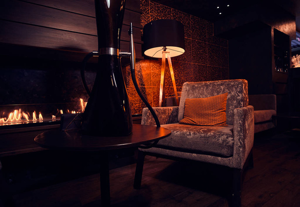 Dark room with working fire place, velvet armchair, lamp and black hookah - Φωτογραφία, εικόνα