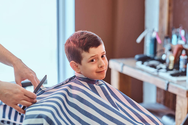 Carino bambino sta ottenendo taglio di capelli alla moda dal barbiere presso il barbiere occupato
 - Foto, immagini