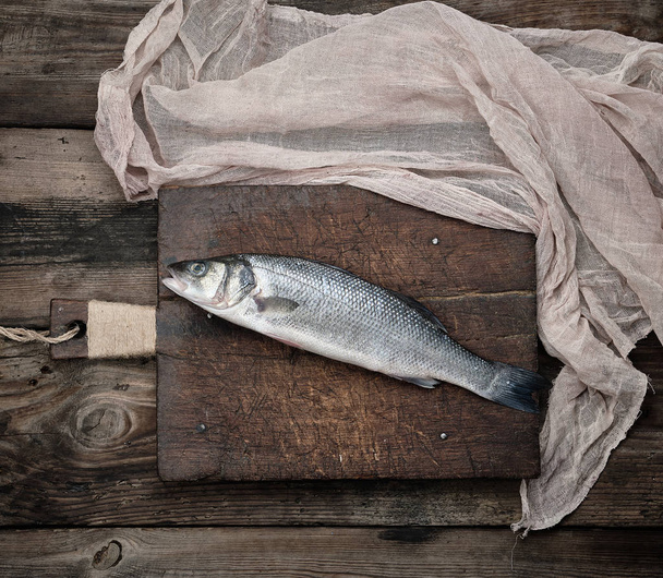 свіжа ціла морська басова риба на коричневій дошці для різання
  - Фото, зображення