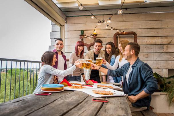 Group of happy friends bonding at home - Young adults having lunch and spending time together on a rooftop terrace, eating pizza and snacks - Fotoğraf, Görsel