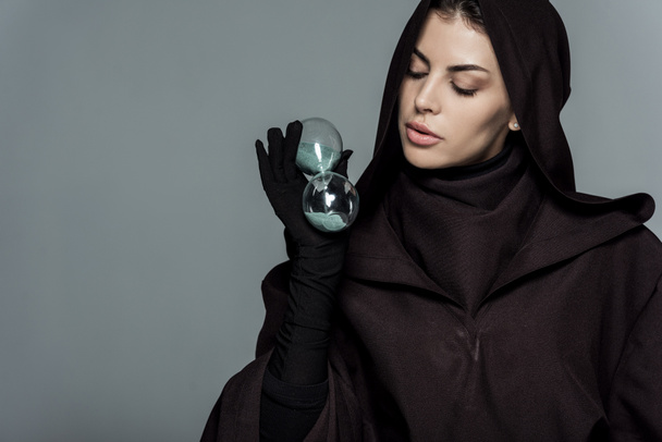 woman in death costume holding sandglass isolated on grey - Photo, Image