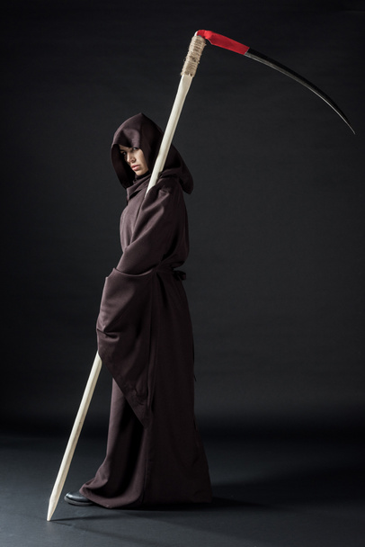 full length view of woman in death costume holding scythe on black - Photo, Image
