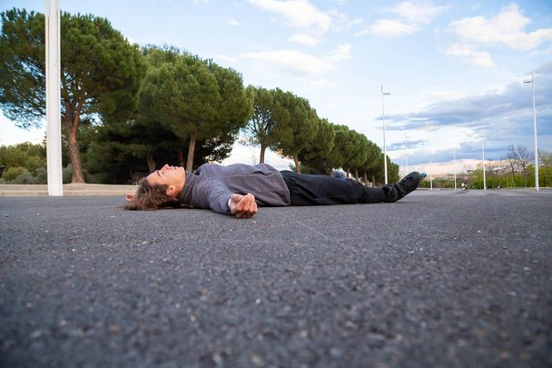 Young fit weary man in sportswear with roller skates lying on road in beautiful city park - Photo, Image
