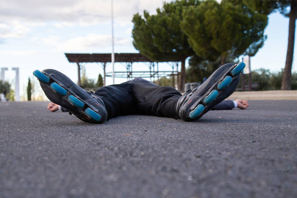 Молодий втомлений чоловік у спортивному одязі з роликовими ковзанами, що лежать на дорозі в красивому міському парку
 - Фото, зображення