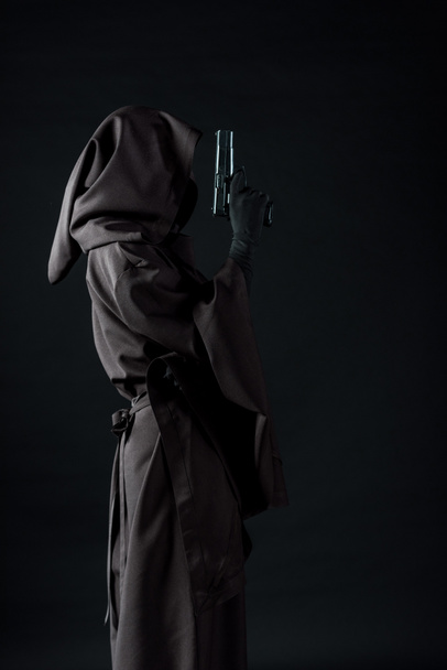 side view of woman in death costume holding gun isolated on black - Photo, Image
