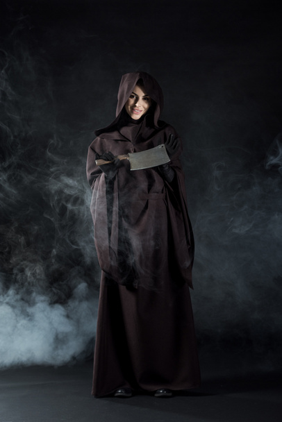 vista completa de la mujer en traje de la muerte sujetando cuchilla en el humo en negro
 - Foto, Imagen