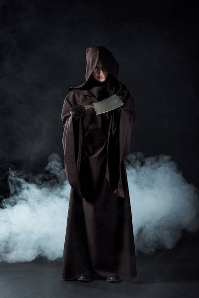 full length view of woman in death costume holding cleaver in smoke on black - Fotografie, Obrázek