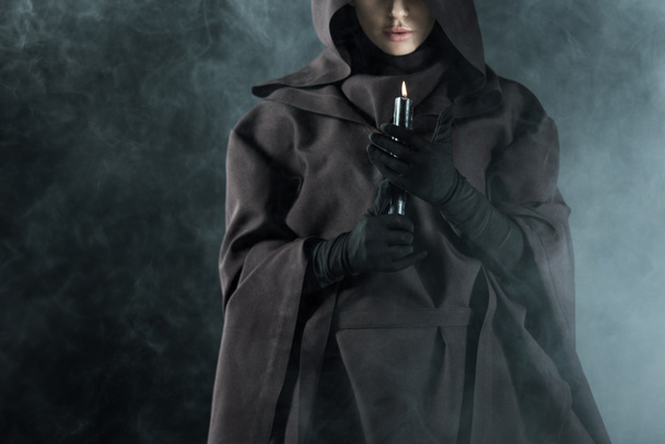 partial view of woman in death costume holding candle in smoke on black - Photo, Image
