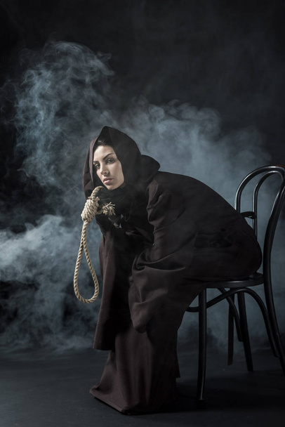 Nainen kuoleman puku istuu tuolilla ja tilalla roikkuu hirttosilmukka musta
 - Valokuva, kuva