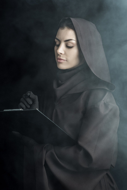 woman in death costume holding clipboard on black - Photo, Image