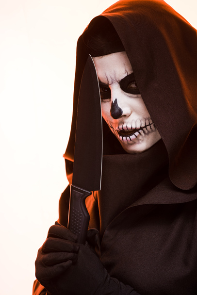 Kafatası makyajlı bir kadın bıçağı beyazın üstünde tutuyor. - Fotoğraf, Görsel