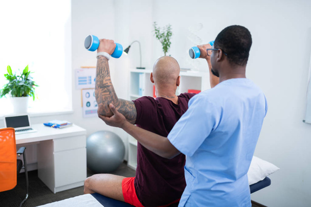 Therapist helping his patient doing exercises with barbells - Foto, afbeelding