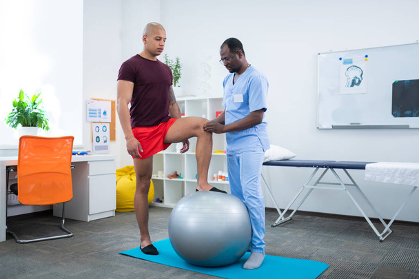 Therapist touching knee of sportsman standing near fit ball - Foto, afbeelding