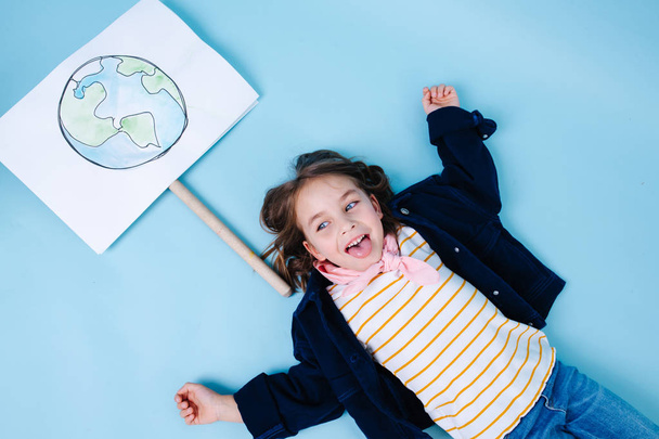 Happy little girl is lying on a floor next to planet earth sign - Foto, Imagem