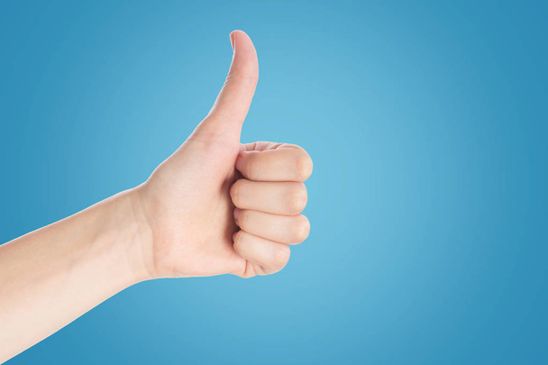 Positive gesture on a blue background. Hand show thumbs up sign, close up - Photo, Image