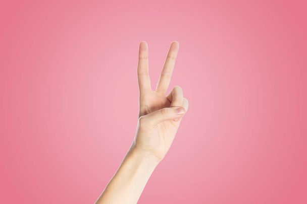 Positive gesture on a pink background. Hand show viktory sign, close up - Foto, Imagem