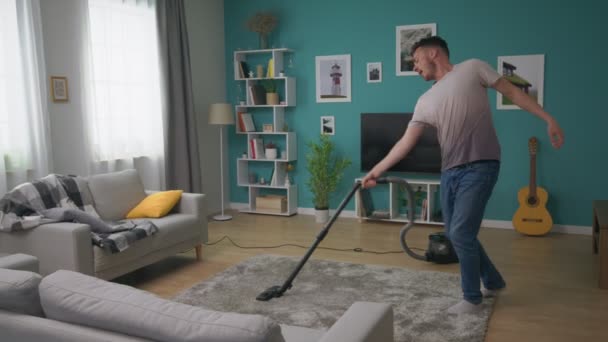 A man vacuums a cozy apartment and dances fun - Materiał filmowy, wideo
