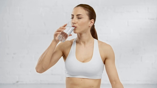attractive woman in sportswear drinking water and looking at camera with smile - Imágenes, Vídeo