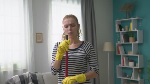 Handheld shot of young woman singing a song using a mop as a microphone - Felvétel, videó