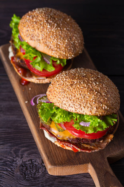 Two delicious homemade beef burgers with bacon on wooden chopping board - 写真・画像