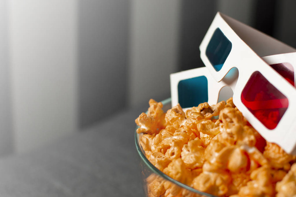 3D glasses and cheesy popcorn lie in a glass plate on a gray bed - Foto, imagen