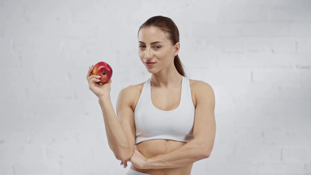 woman with ponytail smiling and showing red apple to camera - Felvétel, videó
