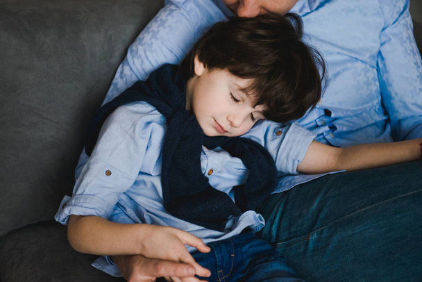 Father with little son sitting on the sofa. Father's day. Happy young father embracing kid sitting on sofa, loving caring dad hugging little boy. Father with little boy using digital tablet at home - 写真・画像